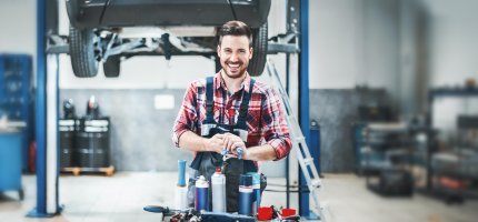 Mann steht in einer Autowerkstatt vor einer Hebebühne