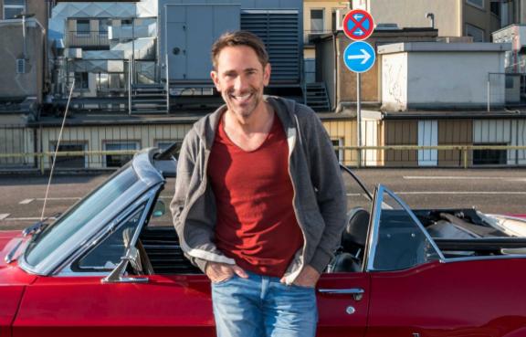 Mann lehnt glücklich an seinem Cabrio am Straßenrand.