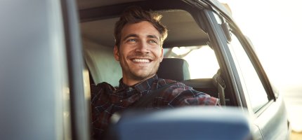 Mann sitzt lächelnd am Steuer und schaut aus dem Fenster