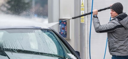 Eine Person wäscht ein Auto mit einem Hochdruckreiniger an einer Waschanlage.
