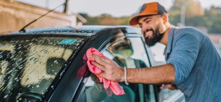 Mann wäscht sein Auto bei Sonnenschein mit einem Lappen