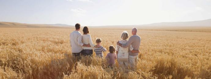 Großeltern, Eltern und Kinder stehen in einem Weizenfeld.