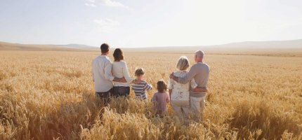 Großeltern, Eltern und Kinder stehen in einem Weizenfeld.