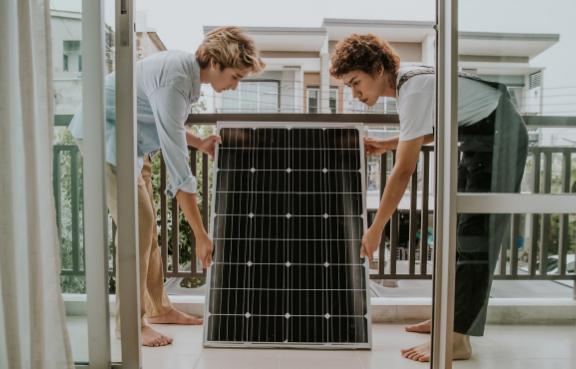 Zwei Frauen tragen ein Solarmodul auf den Balkon.