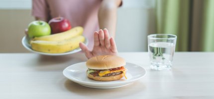 Frau nimmt einen Teller voller Obst und schiebt den Teller mit einem Burger von sich weg.