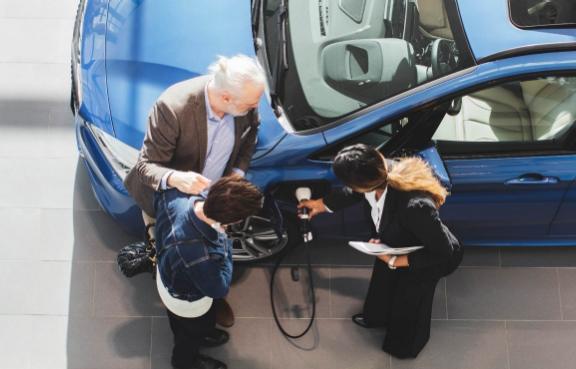 Eine Autoverkäuferin erklärt einem älteren Paar wie man ein Elektroauto lädt.