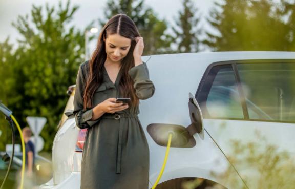 Frau nutzt Handy und wartet auf Ladung ihres weißen E-Autos