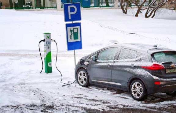 E-Auto steht im Winter vor einer verschneiten Ladesäule und lädt.