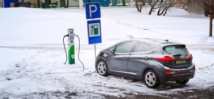 E-Auto steht im Winter vor einer verschneiten Ladesäule und lädt.