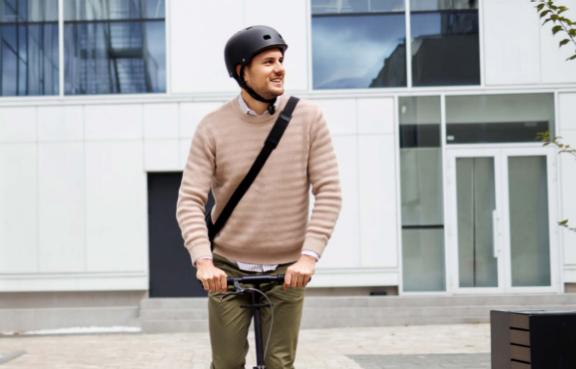 Mann fährt mit einem E-Scooter vor einem Gebäude