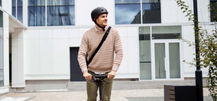 Mann fährt mit einem E-Scooter vor einem Gebäude