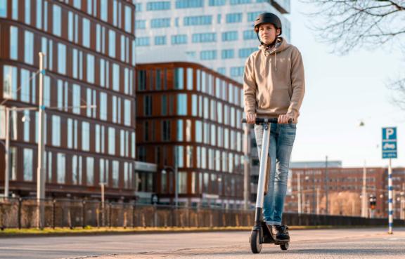 Junger Mann fährt mit einem E-Scooter durch ein Wohngebiet