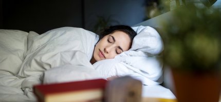 Frau mit geschlossenen Augen im Bett unter einer weißen Decke.