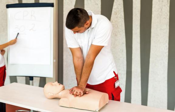 Eine Sanitäterin zeigt auf ein Flipchart und ein Sanitäter macht eine Herzdruckmassage an einer Erste-Hilfe-Puppe.