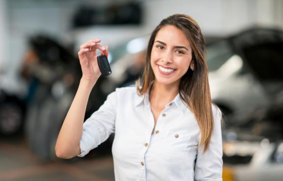 Frau hält in einer Werkstatt einen Autoschlüssel hoch.