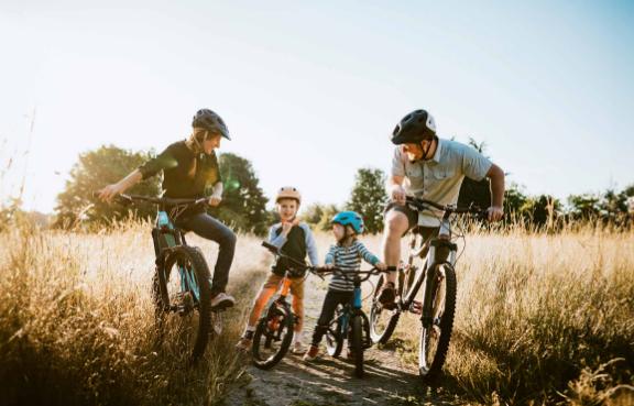 Eine junge Familie hält während ihrer Fahrradtour auf einem Feldweg.