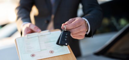 Autokauf, Verkäufer hält Zulassung Papiere und Schlüssel vor einer Reihe an Neuwagen