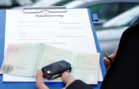 Kaufvertrag für ein Auto auf einem Klemmbrett, darüber ein Fahrzeugschein und ein Autoschlüssel.