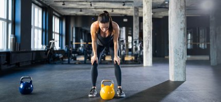 Frau steht im Fitness-Studio über eine Hantel gebeugt.