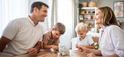 Familie sitzt am Tisch und sortiert Münzen in eine Sparbüchse.