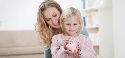 Frau und junges Mädchen halten ein Sparschwein in der Hand