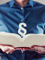 Mann hält ein dickes, aufgeschlagenes Gesetzbuch in den Händen.