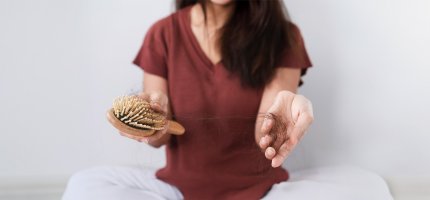 Eine Frau hält eine Bürste in der einen Hand und in der anderen einen Büschel Haare.