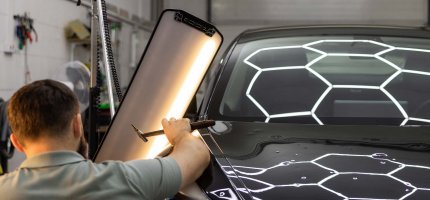 Fahrzeug mit Hagelschaden in der Werkstatt. Mechaniker begutachtet den Schaden.