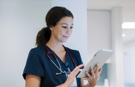 Ärztin steht im Gang und schaut auf ein Tablet.