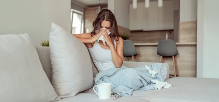 Kranke Frau schnäuzt sich auf der Couch die Nase.