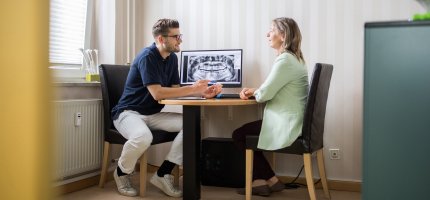 Ein Arzt berät am Schreibtisch eine Patientin.