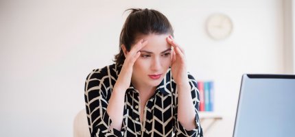 Frau im Büro fasst sich an die Schläfen.