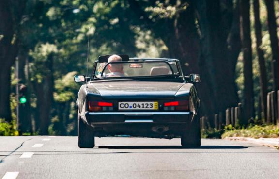 Ein Oldtimer-Cabrio fährt mit offenem Verdeck durch eine Allee.