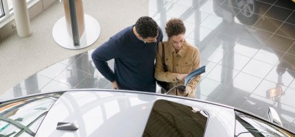 Ein Paar sichtet eine Broschüre neben einem Auto im Autohaus.