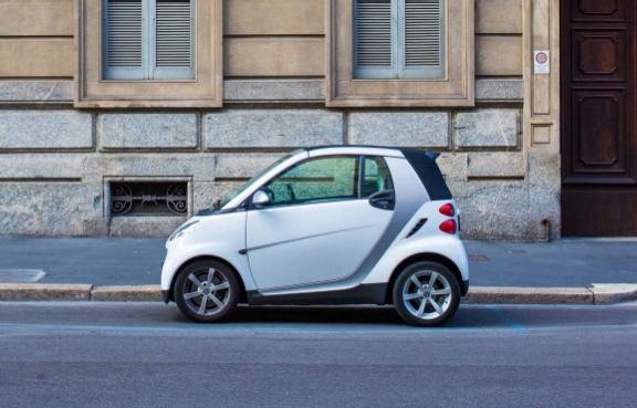 Ein weißes Microcar parkt seitlich in der Stadt am Straßenrand vor einem Haus.