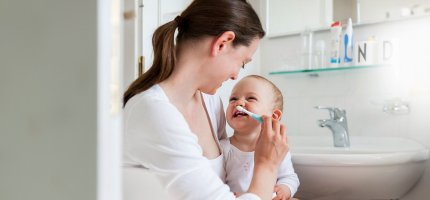 Frau putzt einem Kleinkind die Milchzähne.