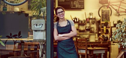 Junge Frau steht in der geöffneten Eingangstür zum Coffee Shop und wartet auf Gäste