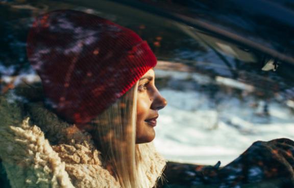 Eine Person sitzt in einem Auto und trägt warme Winterkleidung, während die Sonne durch das Fenster scheint.