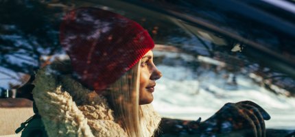 Eine Person sitzt in einem Auto und trägt warme Winterkleidung, während die Sonne durch das Fenster scheint.