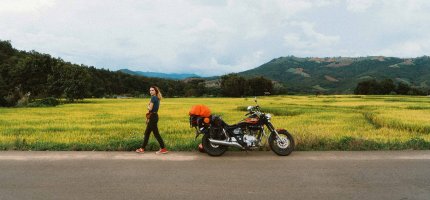 Eine Frau geht von Ihrem am Straßenrand geparkten Motorrad weg.