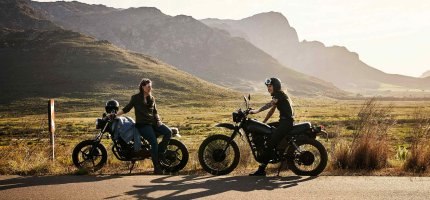 Zwei Motorradfahrer machen vor ein paar Hügeln Pause.