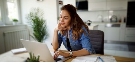 Eine junge Frau sitzt am Laptop. Neben ihr liegen Dokumente.