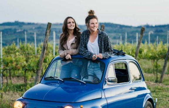 Zwei Frauen schauen aus dem Schiebedach ihres Oldtimer-Kleinwagens.