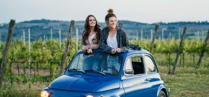 Zwei Frauen schauen aus dem Schiebedach ihres Oldtimer-Kleinwagens.