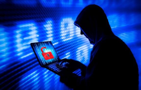 Hacker mit Hoodie schaut in einer dunklen Umgebung auf einen Laptop mit einem roten Schloss.