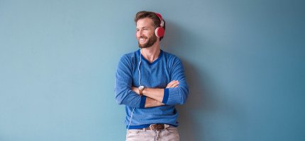 Mann mit Kopfhörern lehnt an einer blauen Wand.