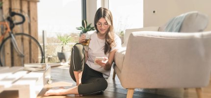 Junge Frau sitzt auf dem Boden und ist am Handy