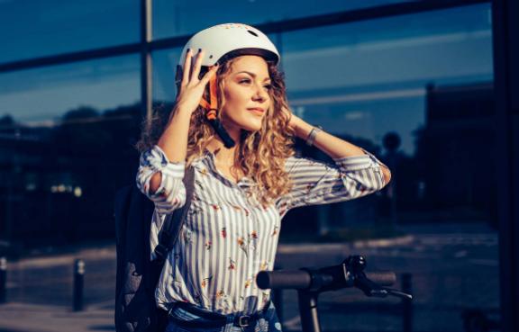Frau steht neben einem E-Scooter und setzt ihren Helm auf
