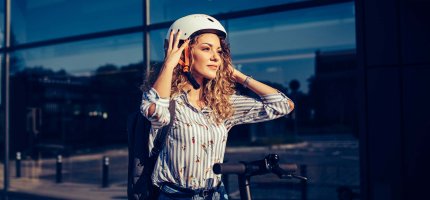Frau steht neben einem E-Scooter und setzt ihren Helm auf