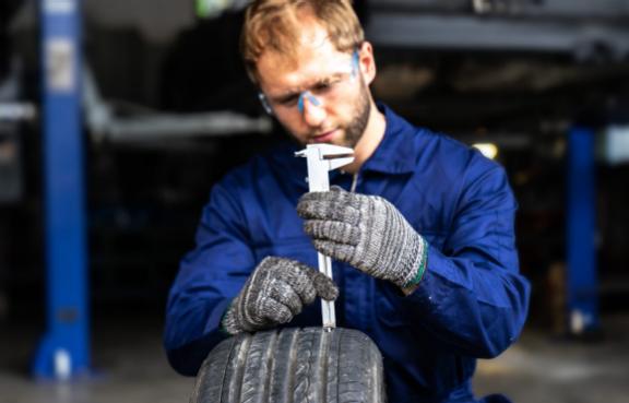 Ein Mechaniker prüft die Profiltiefe eines Autoreifens mit einem Werkzeug.
